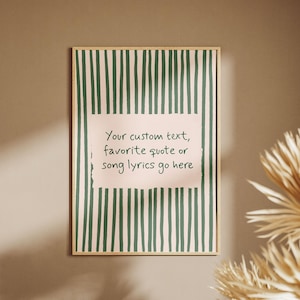 May include: A rectangular wall art print in a light wooden frame featuring a pale pink background with vertical dark green stripes. A central pale pink rectangular block contains the text: Your custom text, favorite quote or song lyrics go here.