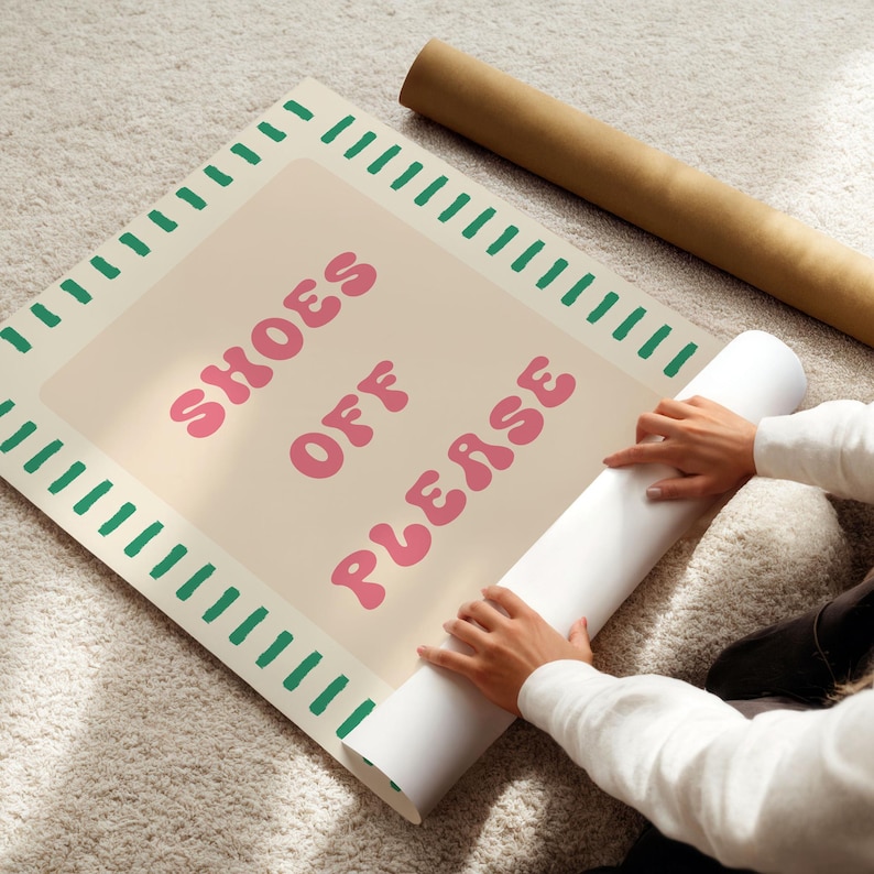 May include: A rectangular poster with a beige background and a green dashed border. The text "SHOES OFF PLEASE" is printed in the center in a pink, rounded, retro-style font. The poster is partially rolled up, revealing a white underside.