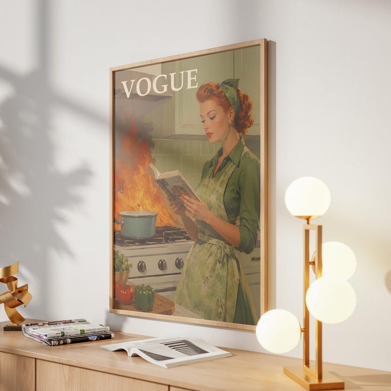 Peut inclure: Impression d'art encadr&eacute;e de style vintage avec une femme en tablier vert lisant un livre dans une cuisine en feu. Le mot "VOGUE" est en haut. Une lampe dor&eacute;e avec des globes blancs est pos&eacute;e sur une surface en bois.