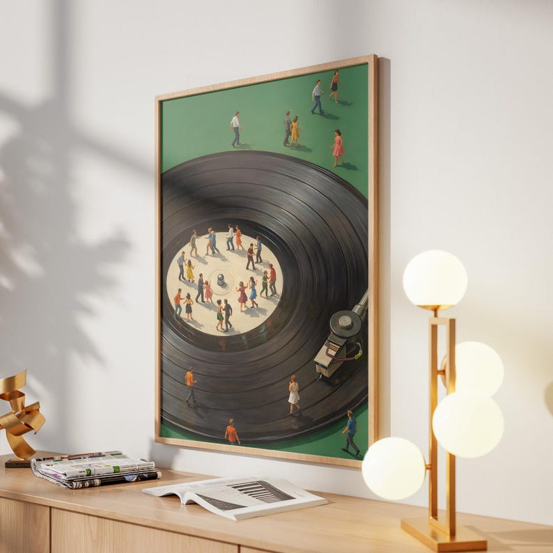 Puede incluir: Una impresi&oacute;n enmarcada que representa un disco de vinilo negro con peque&ntilde;as figuras de personas bailando sobre &eacute;l. El fondo es verde y el marco es de madera clara. Se ve un brazo de tocadiscos. La obra de arte se exhibe en un mueble de madera clara.