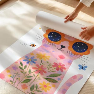 May include: A rolled-up yoga mat featuring a whimsical cat design. The pink cat wears sunglasses and is decorated with colorful flowers, a bee, and a butterfly. The mat is unrolled on a light-colored surface.
