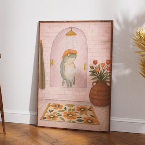 Könnte beinhalten: Gerahmter Kunstdruck mit einer skurrilen Illustration eines Frosches, der duscht. Der Frosch trägt eine orangefarbene Duschhaube unter einem goldenen Duschkopf. Eine Vase mit Tulpen und ein Blummen-Teppich vervollständigen die Badeszene.