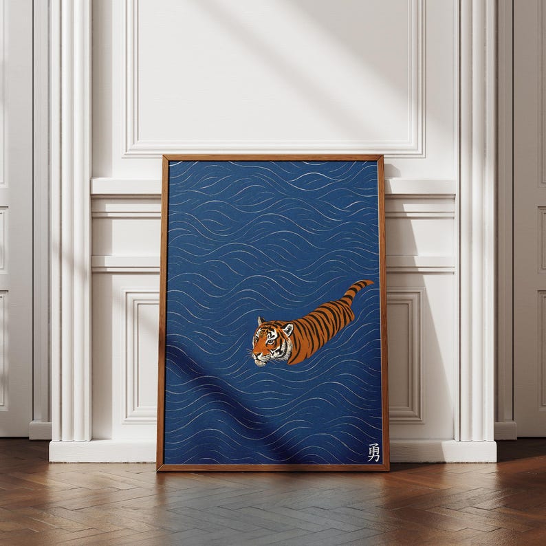 Puede incluir: Una impresi&oacute;n art&iacute;stica enmarcada que presenta un tigre nadando en agua azul con patrones de olas blancas. El tigre tiene rayas naranjas y negras. La obra de arte est&aacute; en un marco de madera y se exhibe contra una pared blanca.