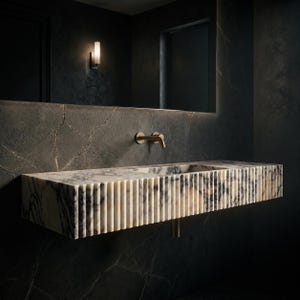 May include: A wall-mounted rectangular bathroom sink crafted from white and grey veined marble. The front and side edges feature a vertical fluted texture. A brass-toned faucet is mounted directly into the dark, cracked-patterned stone wall.