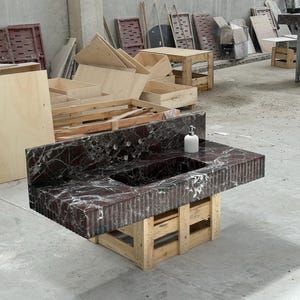 K&ouml;nnte beinhalten: Eine dunkelrote Marmor-Arbeitsplatte mit eingebautem Waschbecken und einem wei&szlig;en Seifenspender. Die Arbeitsplatte wird von einer Holzpalettenbasis getragen. Der Marmor hat wei&szlig;e Adern und eine strukturierte Oberfl&auml;che.