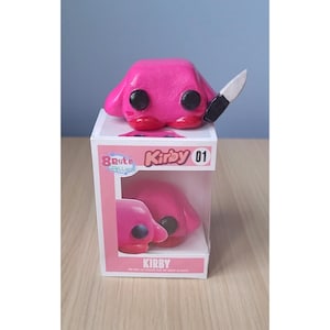 May include: A pink Kirby figure with black eyes and a knife, on a display box. The box says "Kirby 01" and shows a smaller Kirby figure. The figure has a menacing expression.