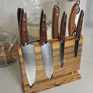 May include: A set of kitchen knives with wooden handles and stainless steel blades, displayed in a wooden knife block. The knives vary in size and shape, with a visible brand name on the blades. The knife block is made of a light-colored wood.