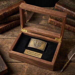 May include: A wooden display case with a glass top, showcasing a vintage U.S. Model 1851 belt buckle. The buckle features an eagle emblem. The case is lined with black velvet and includes a brass nameplate. Antique books are in the background.