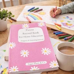 May include: A pink "Parent Record Book For Home Education" journal with white daisy patterns. The journal is on a wooden table with crayons, drawings, and a cup of tea. The journal's cover has the text "Sugar Plum & Co".
