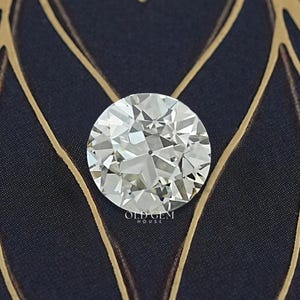 Puede incluir: Un diamante redondo con talla brillante, con múltiples facetas que reflejan la luz. Se encuentra sobre un fondo azul oscuro con un diseño de hojas doradas. La imagen resalta la claridad del diamante.