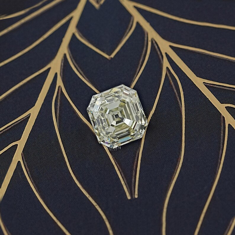 May include: A large, square-cut diamond with a pale yellow hue. The gemstone is set against a dark blue background with gold leaf-like patterns. The diamond's facets reflect light, creating a sparkling effect.