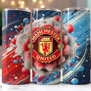 Op de afbeelding: Drie roestvrijstalen bekers met een Manchester United-thema. Elke beker heeft een levendig ontwerp met rode, blauwe en witte abstracte penseelstreken en het logo van het team. Het logo is gecentreerd op een rood en goudkleurig embleem.