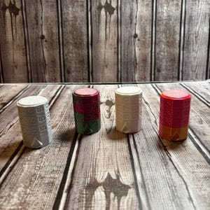 Puede incluir: Cuatro cajas de rompecabezas cilíndricas y coloridas con un diseño numérico. Las cajas son en tonos de gris, rosa, verde, blanco y naranja. Las cajas están dispuestas sobre una superficie de madera.
