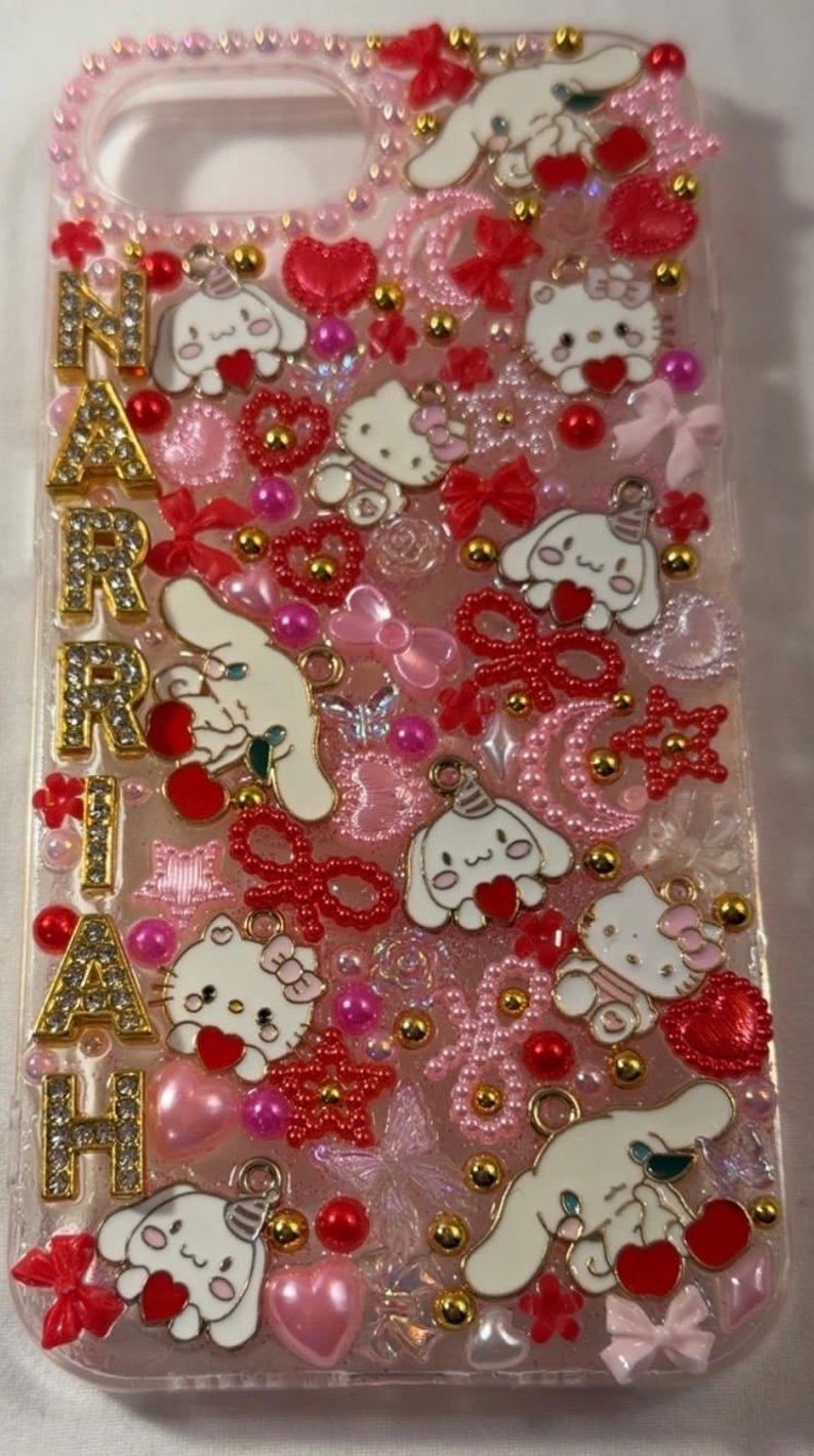 Peut inclure: Une coque de t&eacute;l&eacute;phone rose orn&eacute;e de Hello Kitty, Cinnamoroll, de c&oelig;urs, de n&oelig;uds et d'accents dor&eacute;s. Le nom "MARIAH" est &eacute;pel&eacute; en lettres dor&eacute;es. L'&eacute;tui est orn&eacute; de divers embellissements roses et rouges.