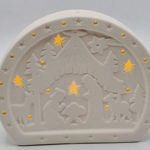 Op de afbeelding: Crèmekleurige, boogvormige kerstversiering met een uitgesneden kerststal. De scène toont figuren, bomen en sterren, met kleine gele lampjes die het ontwerp verlichten. De decoratie heeft stervormige uitsparingen langs de rand.