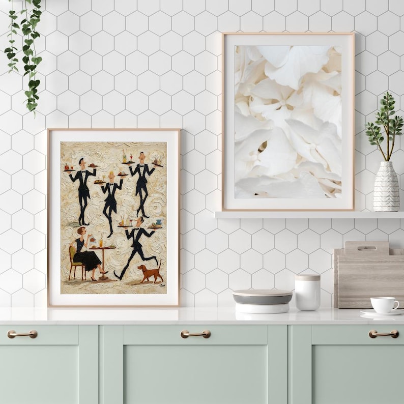 May include: Two framed art prints. One features a painting of waiters in black suits carrying trays, a woman at a table, and a dog. The other print is a close-up of white flower petals. The prints are displayed above a mint green cabinet.