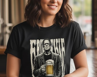May include: A black short-sleeve t-shirt featuring a graphic print of a figure resembling Frankenstein's monster wearing a jacket and holding a glass of beer, with the text "FRANKENSTEIN" printed in a distressed, vertical font above the figure.