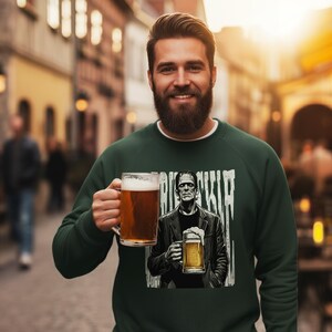 May include: A dark green long-sleeve sweatshirt featuring a graphic print of a character resembling Frankenstein's monster holding a beer mug, with the text "FRANKENSTEIN" partially visible in a distressed white font above the character.