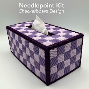 May include: Needlepoint tissue box cover with a checkerboard design in shades of purple. The box has a dark purple border and a rectangular opening for tissues. White tissues are visible.