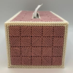 May include: A rectangular tissue box cover in a dusty rose color, featuring a woven pattern. The edges are trimmed with a cream-colored border. A white tissue is partially pulled from the top opening. The cover is handmade.