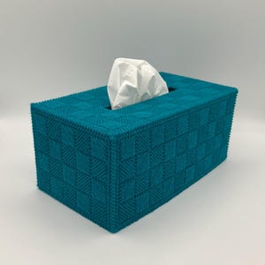 May include: Teal tissue box cover with a woven pattern. The rectangular box has a square pattern design and a rectangular opening at the top for tissue dispensing. White tissues are visible.