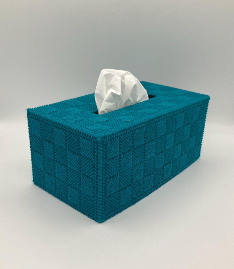 May include: Teal tissue box cover with a woven pattern. The rectangular box has a square pattern design and a rectangular opening at the top for tissue dispensing. White tissues are visible.