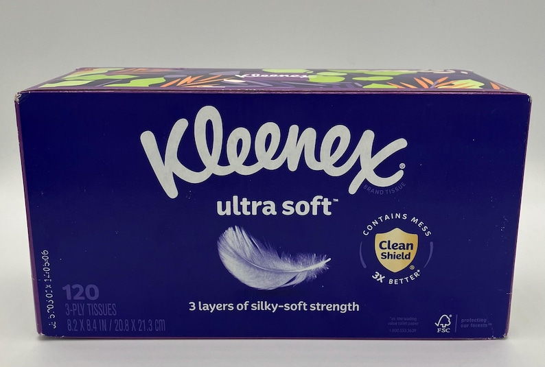 Puede incluir: Una caja rectangular de pa&ntilde;uelos Kleenex Ultra Soft en color morado oscuro. El frente presenta el nombre de la marca, un gr&aacute;fico de pluma blanca y texto que indica 120 pa&ntilde;uelos de 3 capas, 20,8 x 21,3 cm y un logo Clean Shield de protecci&oacute;n.