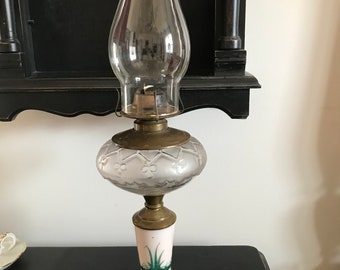 May include: Antique oil lamp with a clear glass chimney, a frosted glass globe with a floral pattern, a white porcelain base with green floral accents, and a black wooden base.