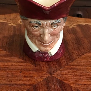 Op de afbeelding: Een keramiek beeldje van een mannenhoofd met een rode hoed. Het beeldje is een traditionele Engelse Toby Jug.