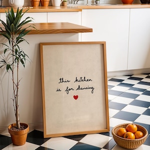 Może przedstawiać: Oprawiony wydruk z napisem "this kitchen is for dancing" i czerwonym sercem. Wydruk opiera się o ścianę obok rośliny doniczkowej i kosza pomarańczy. Podłoga ma czarno-biały wzór w szachownicę.