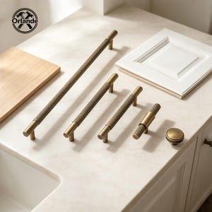 May include: A collection of antique brass cabinet hardware including four cylindrical bar pulls with a textured knurled finish and one matching round knob. The hardware is arranged in a row, showcasing varying lengths from long to short.