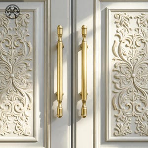 May include: Close-up of a pair of gold-colored door handles with a vertical bar design. The handles are mounted on a white door with ornate, floral relief carvings. The brand name "Orlande" is visible in the upper left corner.