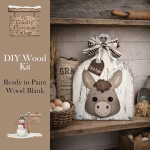 May include: A DIY wood kit with a donkey face design. The kit includes a ready-to-paint wood blank with a distressed white finish, a decorative bow, and a tag that says "hee-haw". The Country Christmas Cottage logo is visible.