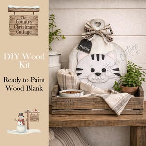 May include: A wooden cat-shaped DIY kit with a "meow" tag, set in a wooden crate with a bowl of food and a striped towel. The kit is ready to paint. The Country Christmas Cottage logo is visible.