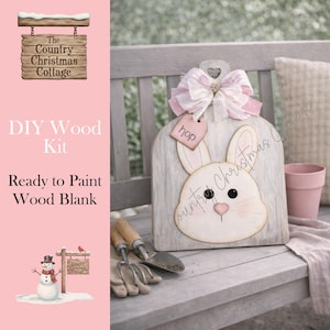 May include: A DIY wood kit featuring a bunny face design, ready to paint. The bunny is on a wooden board with a pink bow and a tag that says "hop". The kit is for a craft project. The text "The Country Christmas Cottage" is visible.