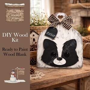 May include: DIY wood kit featuring a skunk design. The wooden blank is painted white with a black and white skunk face. A black and white checkered bow and a tag that says "stinker" are attached to the top. The text "DIY Wood Kit" and "Ready to Paint Wood Blank" are also visible.