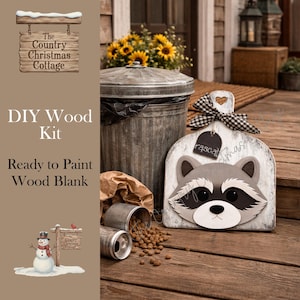 May include: A DIY wood kit with a raccoon design. The kit includes a ready-to-paint wood blank with a raccoon face, a black and white checkered ribbon, and a tag that says "rascal". The kit is from The Country Christmas Cottage.
