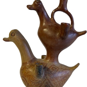 May include: A brown ceramic vessel shaped like two stacked ducks. The lower duck features intricate geometric and floral patterns in darker brown tones. The upper duck has a hollow handle and a spout extending from its back, creating a functional form.
