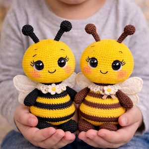 Può includere: Due peluche a forma di ape fatti a mano all'uncinetto. Le api hanno corpi gialli con strisce nere e marroni, occhi grandi e piccole ali. Ogni ape ha una faccia sorridente e un colletto decorativo. I peluche sono tenuti tra le mani di una persona.