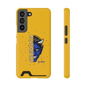May include: Mustard yellow phone case featuring a blue devil graphic with the text "BLUE DEVILS" and "OLD FORGE". The case has a black camera module and buttons on the side. The design is a bold, eye-catching statement.