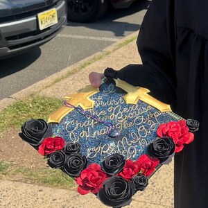 May include: A decorated graduation cap with the text "Trust the Next Chapter Because You Know the Author". The cap is blue with gold accents and adorned with black and red paper roses.