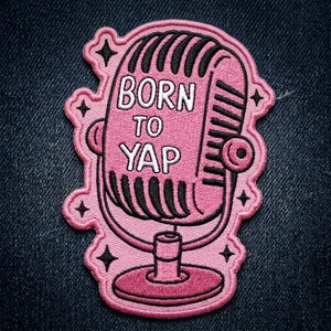 May include: Pink embroidered patch featuring a vintage microphone design. The patch has the words "BORN TO YAP" in white lettering. The patch is outlined in pink with black accents and four small star shapes.