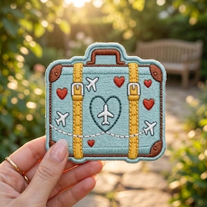 May include: Embroidered patch in the shape of a suitcase, featuring a light blue background with brown trim and yellow straps. The design includes red hearts, white airplanes, and a heart-shaped airplane graphic. A travel-themed accessory.