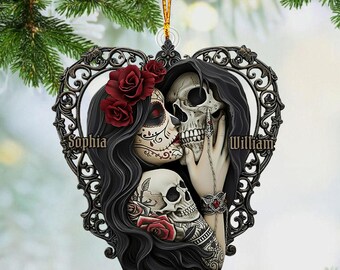 May include: A heart-shaped ornament featuring a Day of the Dead couple kissing, with a skull and rose design. The ornament has the names "Sophia" and "William" and the text "PERSONALIZED DESIGN". The ornament is hanging from a gold string.