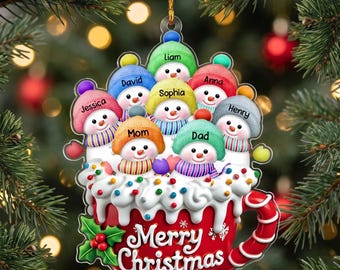 May include: A flat Christmas ornament shaped like a red mug filled with whipped cream and seven snowmen. Each snowman wears a colorful hat and is labeled with the names Liam, David, Jessica, Mom, Dad, Sophia, Anna, and Henry. The mug says Merry Christmas.