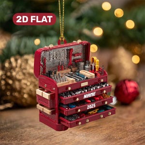 May include: A red toolbox ornament with multiple drawers and tools. The ornament has the text "NAME" and "2025" on the drawers. The ornament is hanging from a gold string. The text "2D FLAT" is on the top left.