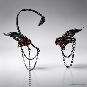 Pode incluir: Um ear cuff e um anel a condizer em metal preto com motivos de rosas de pétalas vermelho-escuras. O ear cuff tem uma estrutura curva semelhante a uma trepadeira com um detalhe de pena e correntes pendentes. O anel também inclui uma pena.