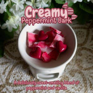 May include: A white ceramic wax warmer filled with red heart-shaped wax melts and peppermint bark pieces. The text "Creamy Peppermint Bark" and "A deliciously sweet-smelling blend of peppermint and vanilla" are displayed.