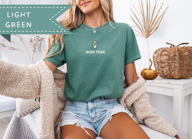 May include: A light green t-shirt with the text "IRISH YOGA" and a graphic of a coffee cup with a shamrock. The shirt is paired with denim shorts. A light-colored sweater is draped over the shoulders.
