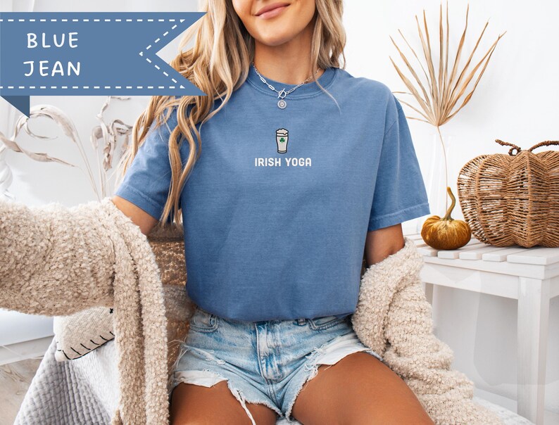 May include: Blue jean colored t-shirt with the text "IRISH YOGA" and a coffee cup graphic. The shirt has short sleeves and a crew neck. A blue banner with the words "BLUE JEAN" is in the upper left corner.